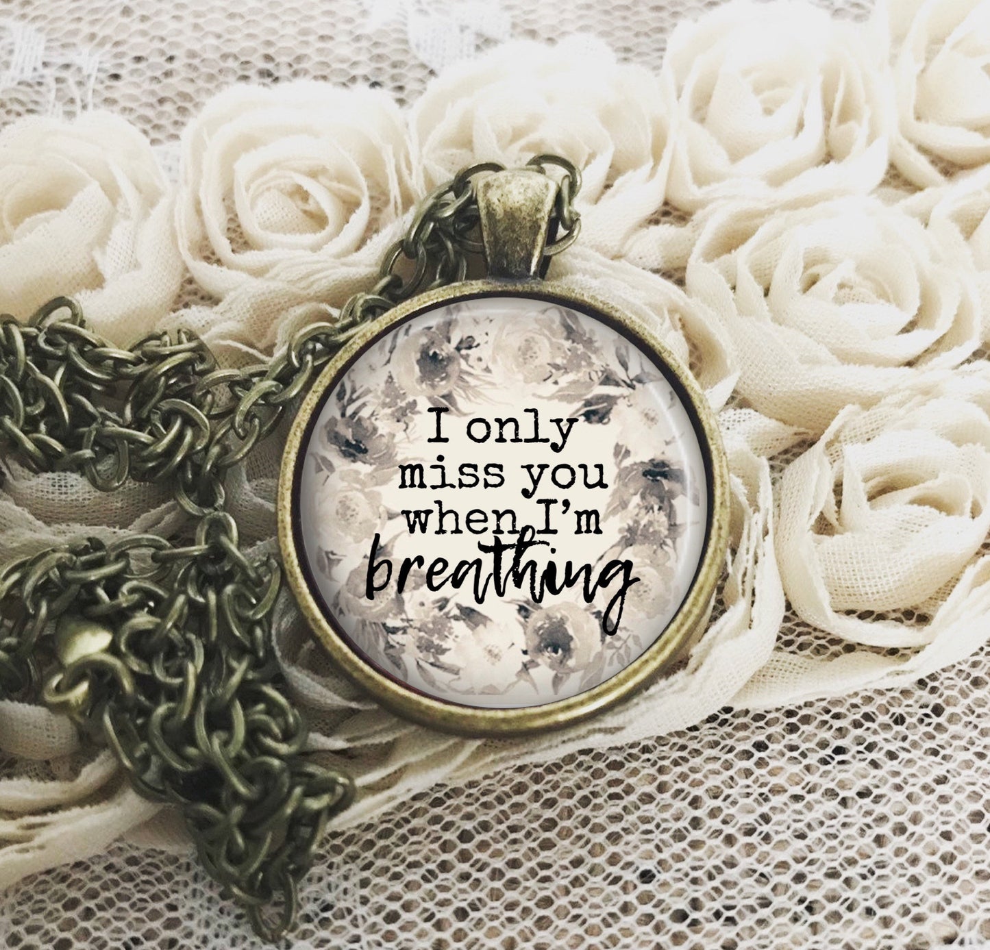 A necklace with a round pendant featuring a floral design and the text &#39;I only miss you when I&#39;m breathing&#39;.